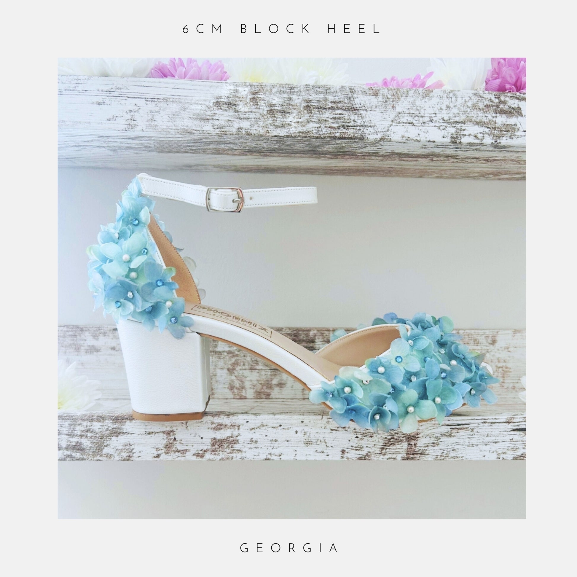 Ivory peep toe block heel bridal sandal with blue floral embellishments on a wooden surface with flowers.