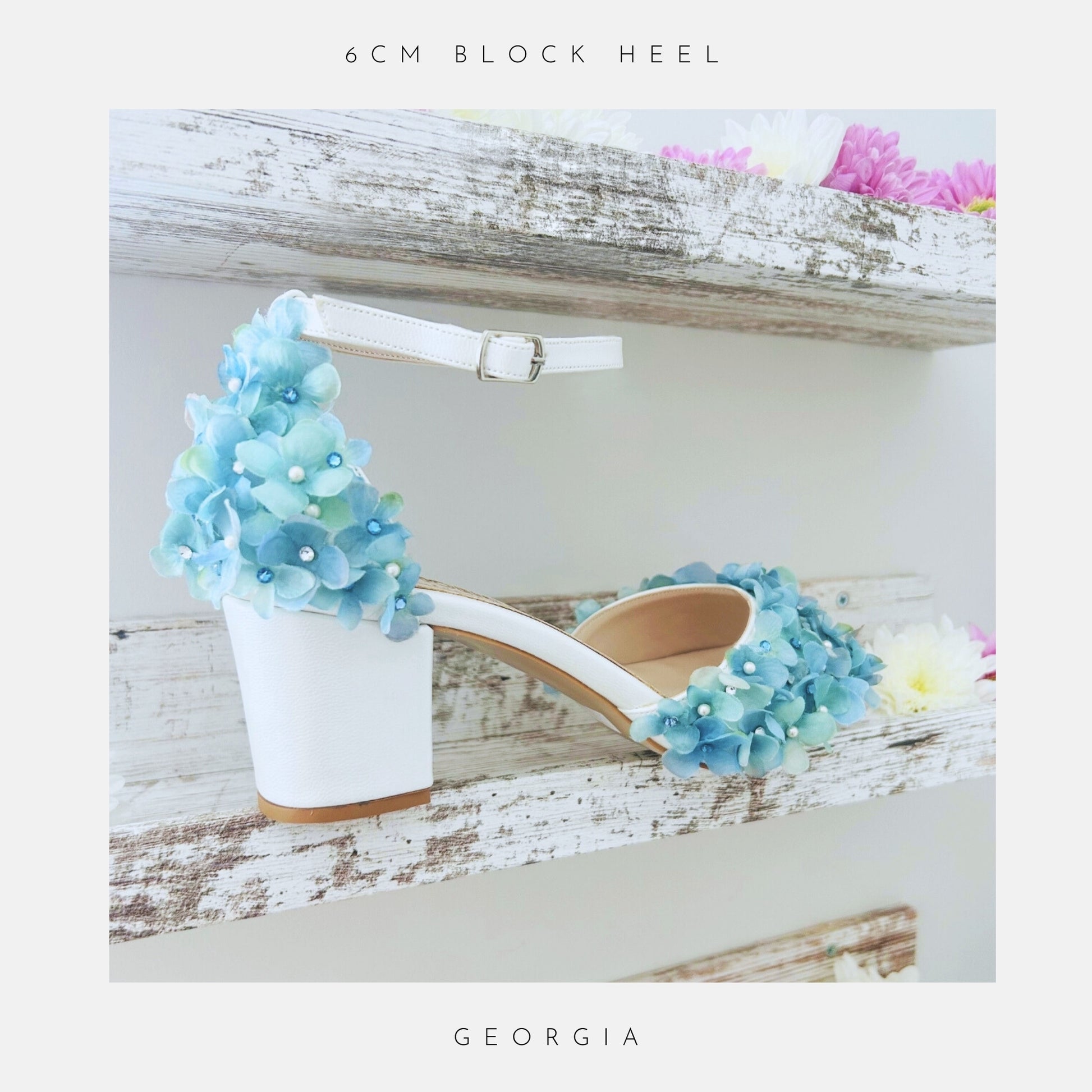 Ivory low block heel wedding sandal with blue floral decorations on a wooden surface with flowers.