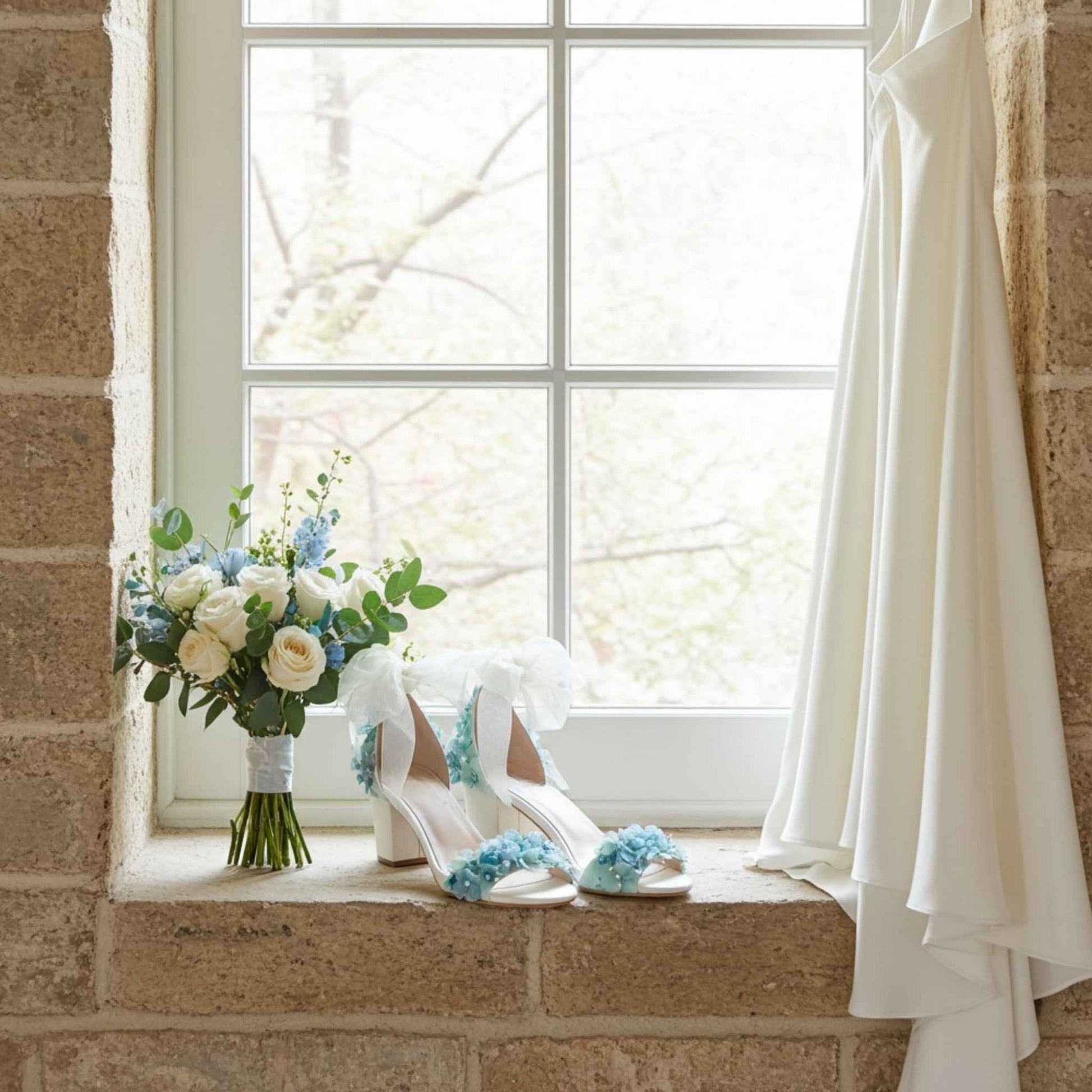 Bridal shoes with blue floral decorations and a bouquet on a stone window sill.