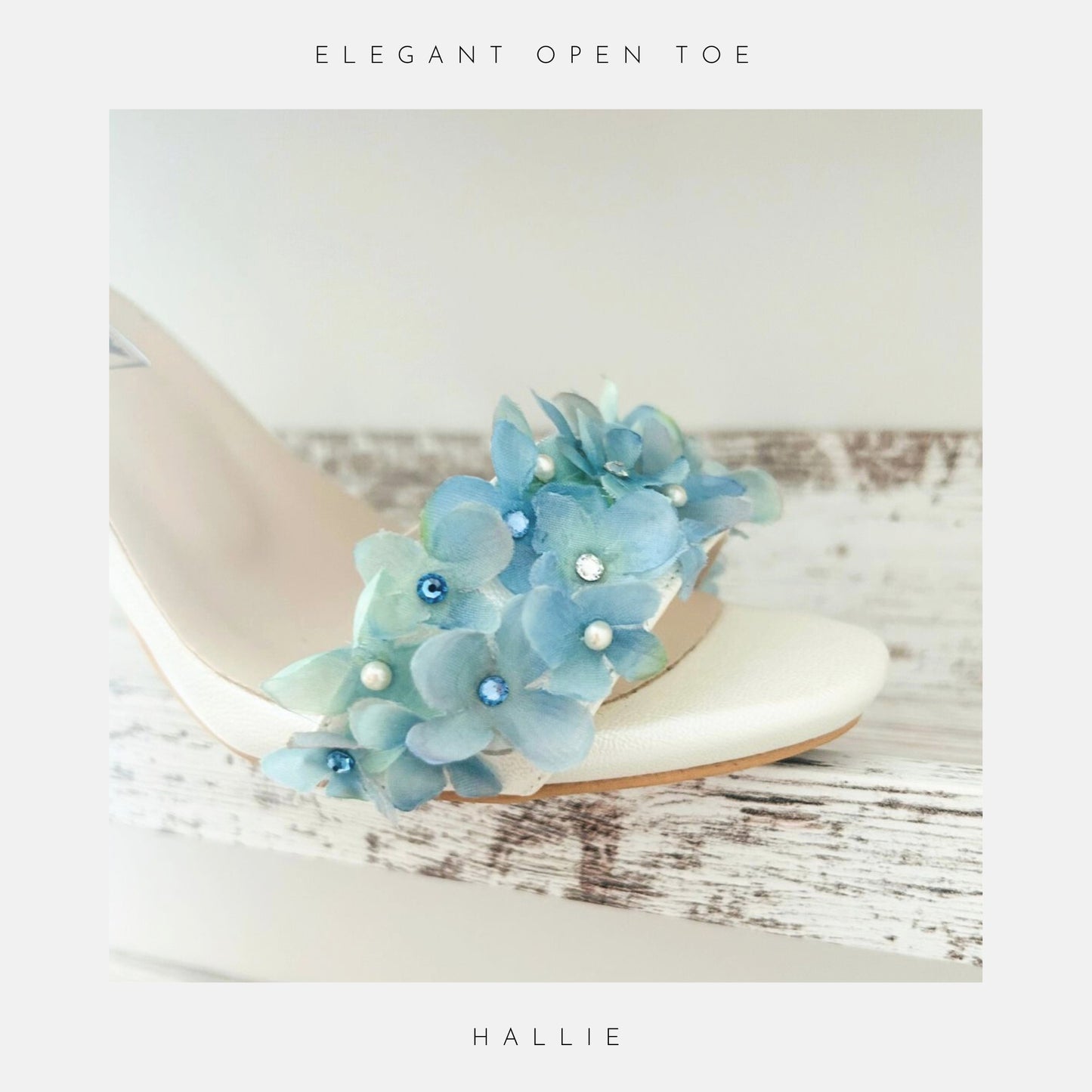 Ivory bridal sandal with blue floral decorations on a light wooden surface, labelled 'Elegant Open Toe' and 'Hallie'.