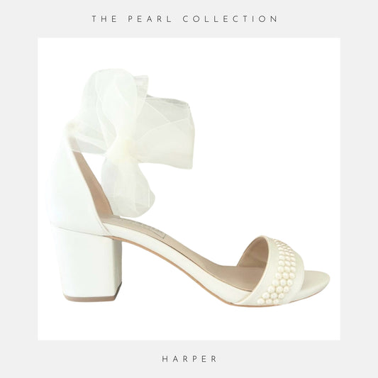 Low block heel open toe bridal shoe finished with pearls and an organza strap on white bordered background.