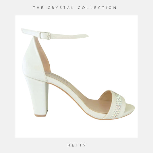 Ivory sandal with block heel and pearl embellishments on a light grey background, labelled 'Hetty' and 'The Crystal Collection'.
