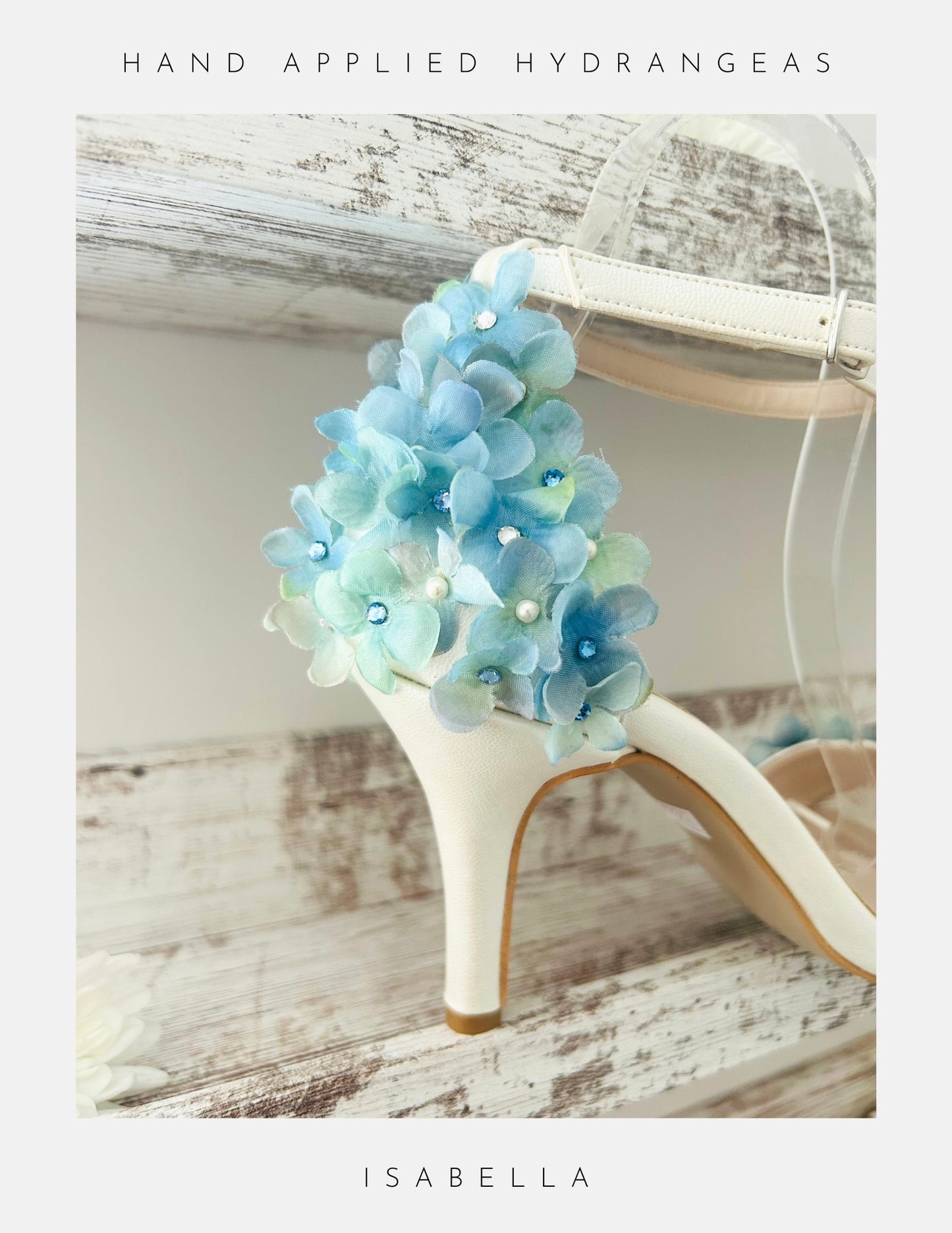 Ivory floral high-heeled wedding shoe with blue hand-applied hydrangeas on a wooden surface.