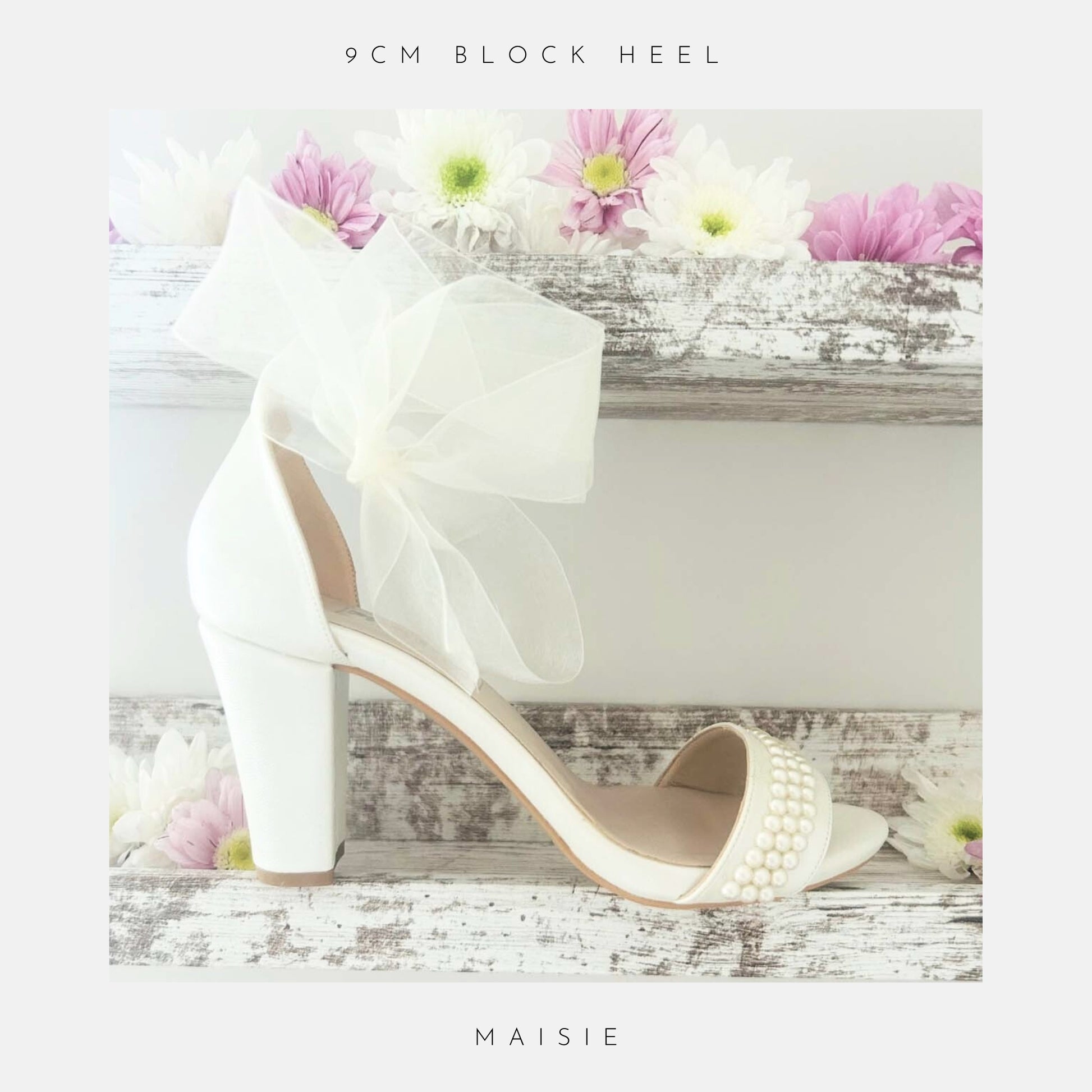 Ivory high-heeled bridal shoe with a decorative bow and pearl details on a wooden surface with flowers.