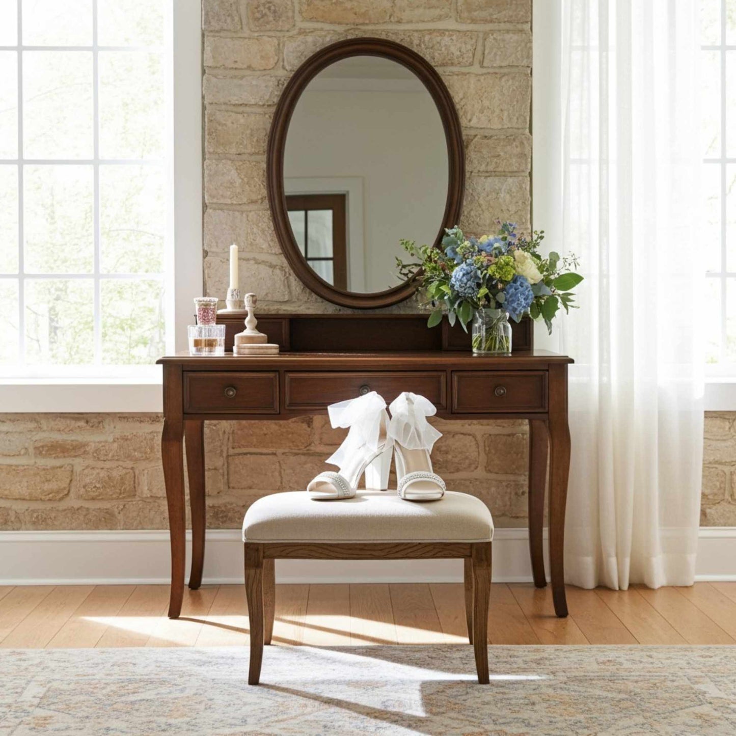 Wooden vanity with mirror, open toe shoes on a stool, and flowers in a room with stone wall and window.