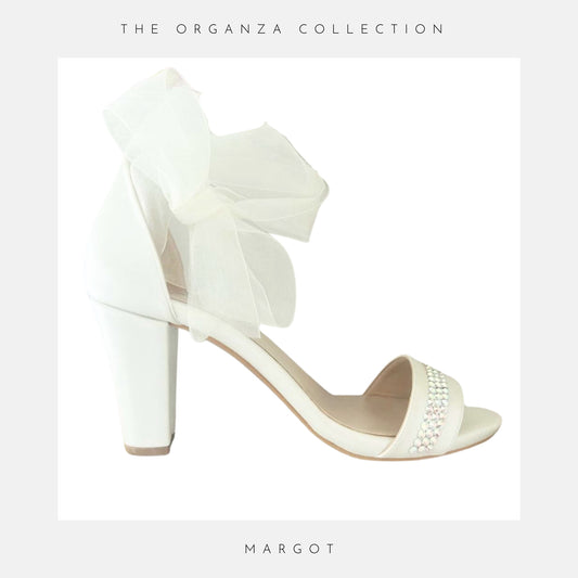Ivory bridal sandal with a large bow on a light grey background, labelled 'The Organza Collection' and 'MARGOT'.