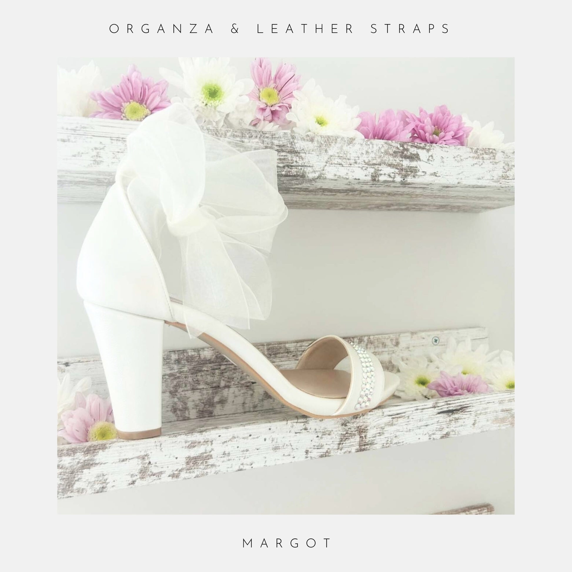 Ivory high-heeled block heel bridal shoe with an organza bow on a wooden surface with flowers, branded 'MARGOT'.