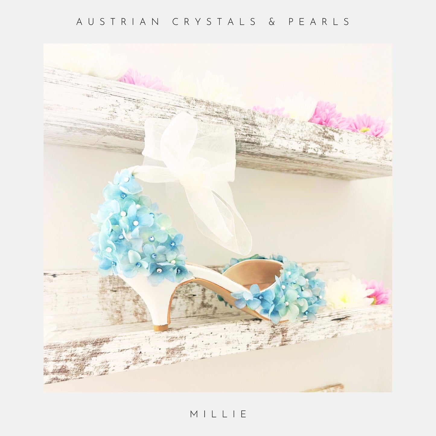 Ivory high-heeled shoes with blue floral embellishments on a wooden surface with flowers.