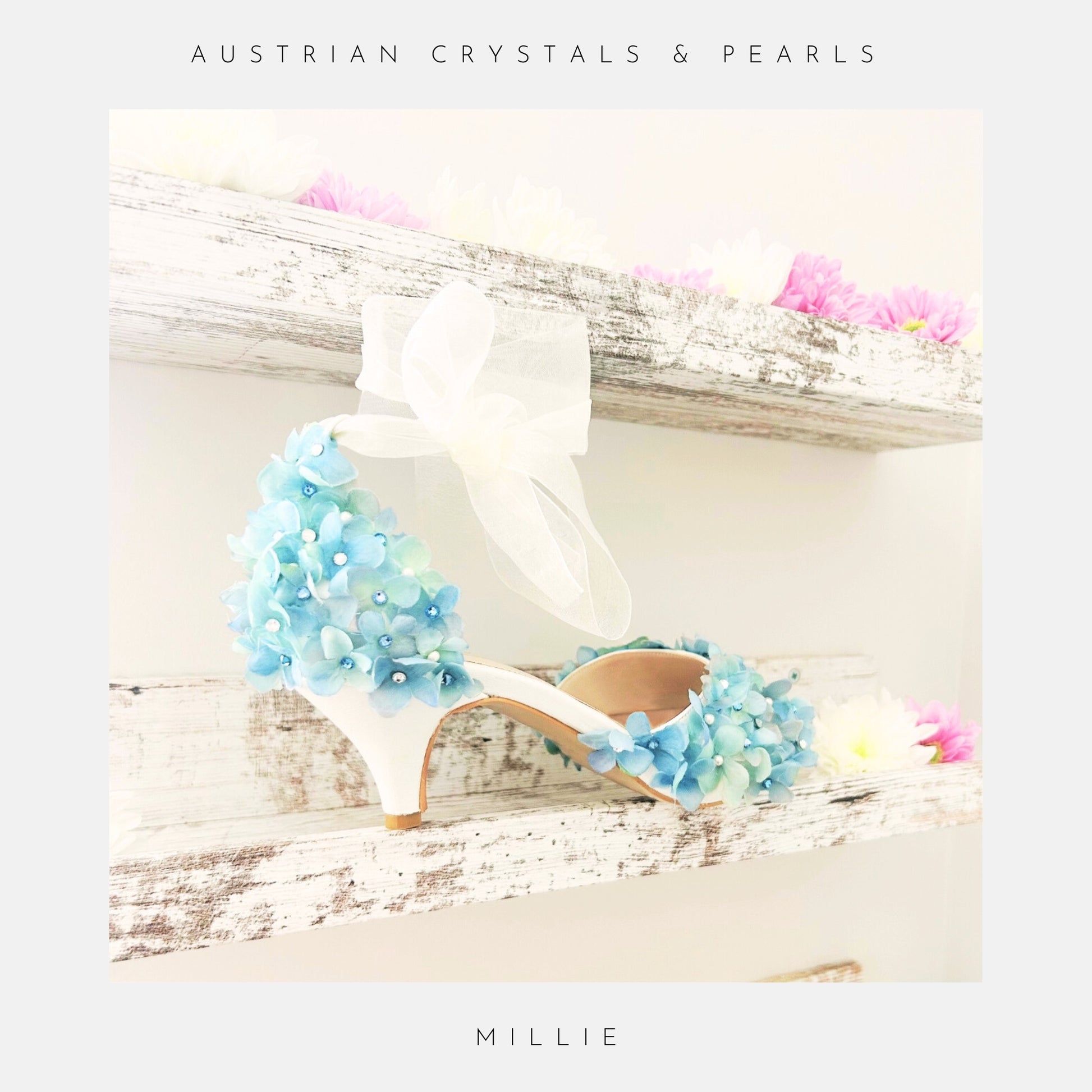 Ivory high-heeled shoes with blue floral embellishments on a wooden surface with flowers.