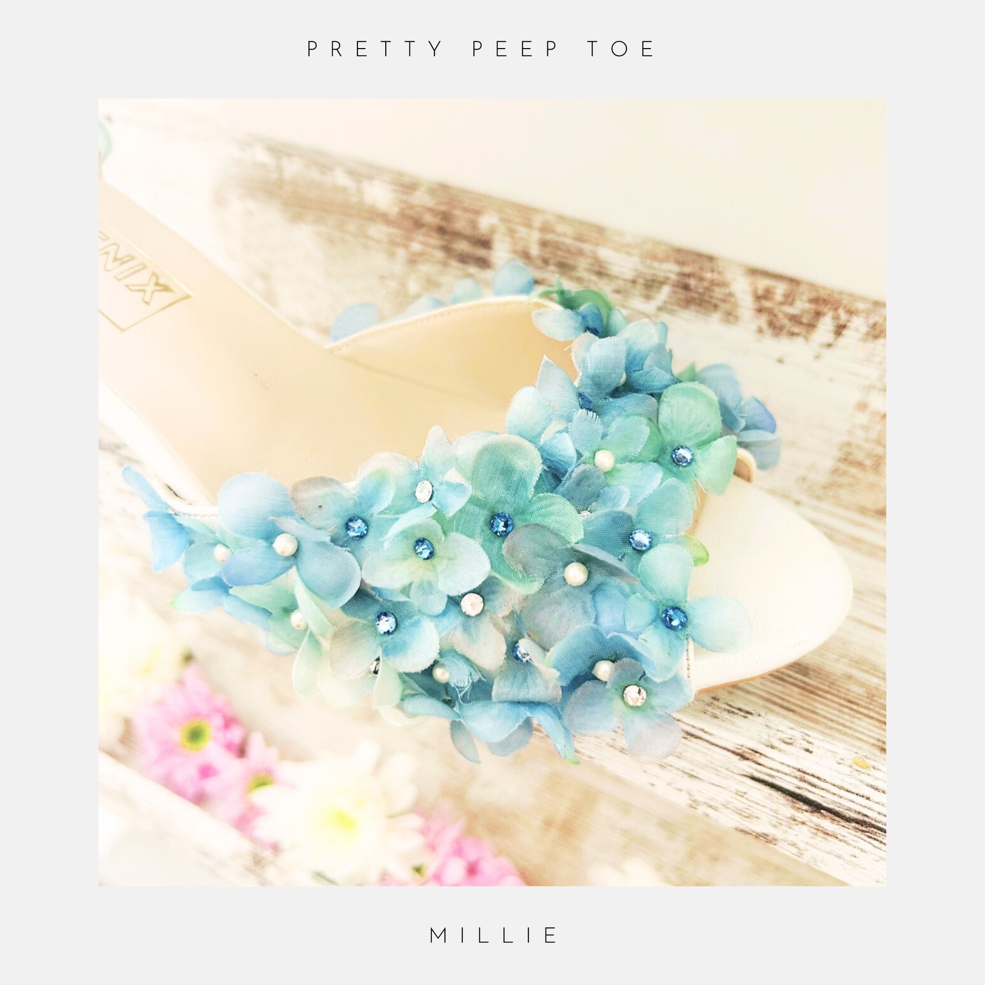 Ivory peep toe bridal sandal with blue floral embellishments on a wooden surface.