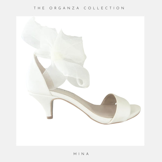 Ivory sandal with ruffled design on a light grey background, featuring 'The Organza Collection' and 'Mina'.
