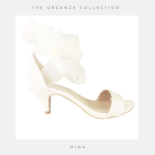 Ivory open toe bridal sandal with ruffled bow design on a white background, part of 'The Organza Collection' by Mina.