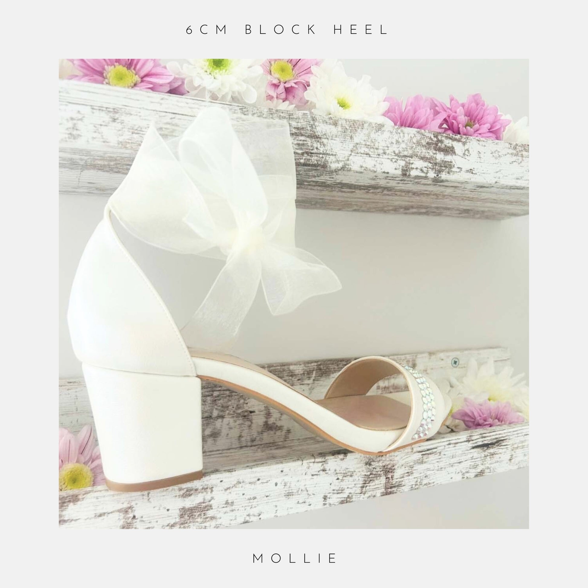 Ivory wedding shoe with an organza bow on a wooden surface with flowers