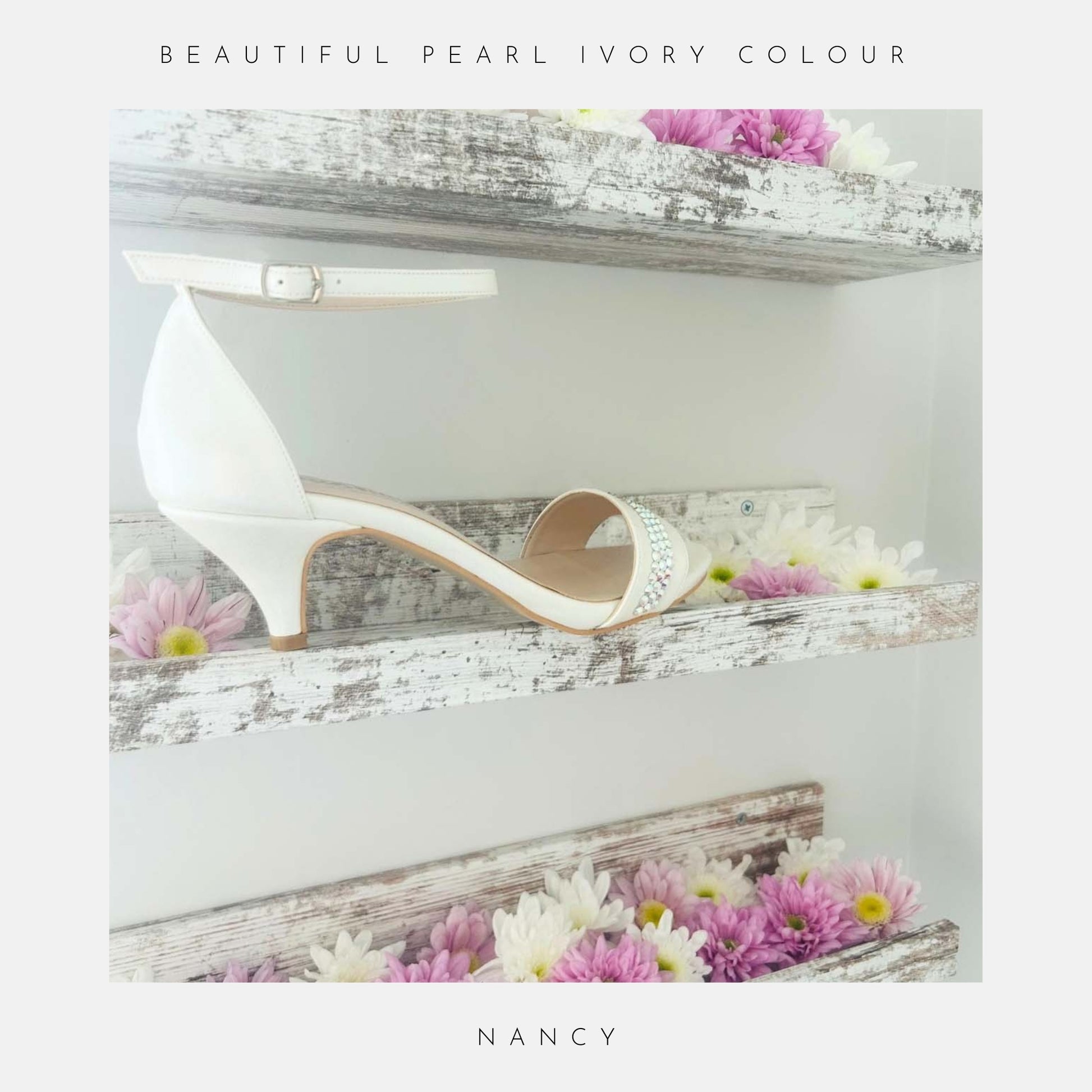 A pair of Nancy Crystal Kitten Heel Bridal Shoes by Phoenix England, in pearl vegan leather with ankle strap, is displayed on rustic white shelves adorned with daisies. Text above reads STUNNING IVORY PEARL COLOUR and below, NANCY.
