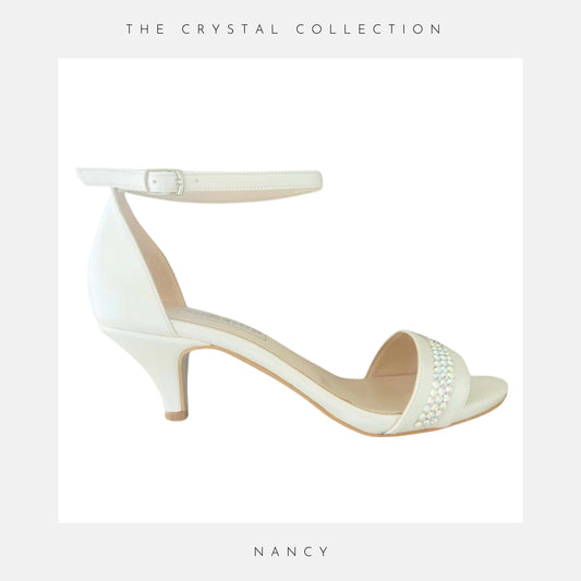 Ivory high-heeled shoe with pearl embellishments on a light grey background, labelled 'Nancy' under 'The Crystal Collection'.