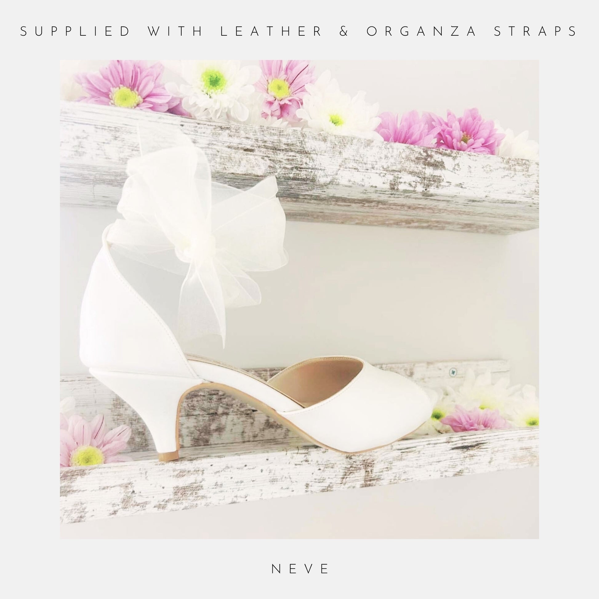 Ivory wedding shoe with a bow and kitten heel on a wooden surface with flowers, labelled 'Supplied with leather and organza straps' and 'Neve'.