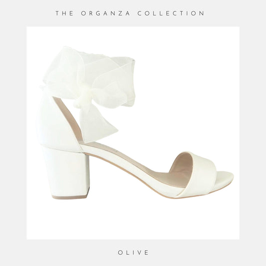 Ivory bridal sandal with a low block heel on a light grey background, part of 'The Organza Collection'.