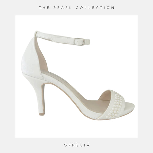 Ivory high-heeled open toe wedding shoes with pearl embellishments on a wooden surface, labelled 'The Pearl Collection'.