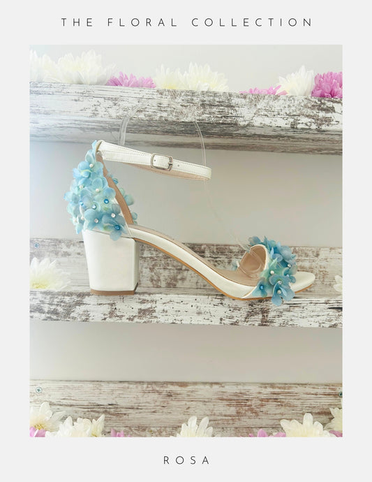 The Rosa Floral Low Block Heel Bridal Shoes by Phoenix England—a white sandal with blue and white flower appliqués, ankle strap, and low block heel—perfect for your special day. The Floral Collection.