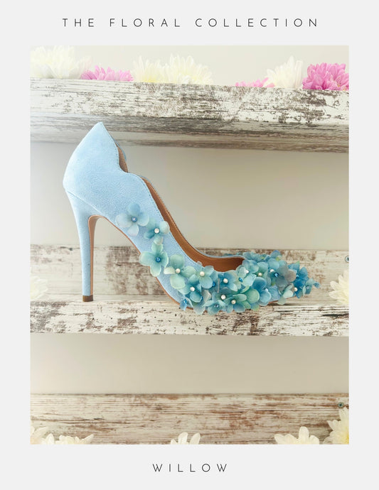 Blue high-heeled bridal shoe with floral decorations on a wooden surface, labelled 'The Floral Collection' and 'Willow'.