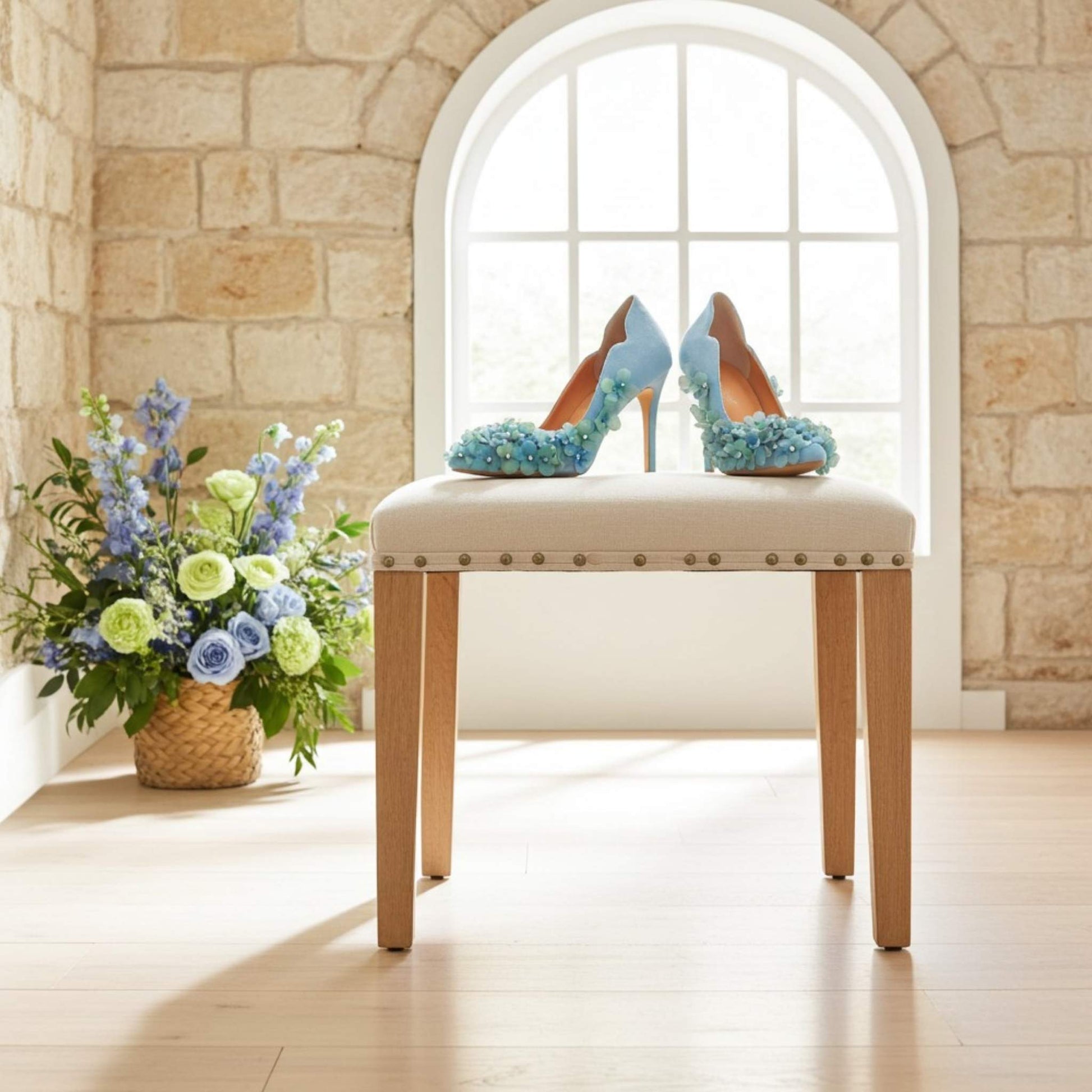 Decorative blue floral high-heeled court shoes on a stool with a floral arrangement in the background.