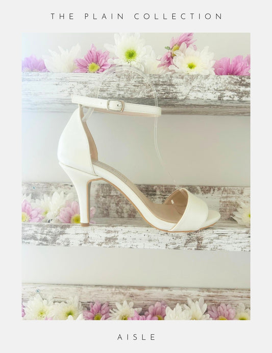 An open toe high heel ivory bridal shoe shown on a shelf with pretty flowers.