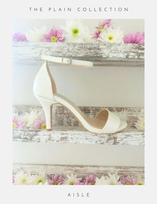 An open toe high heel ivory bridal shoe shown on a shelf with pretty flowers.