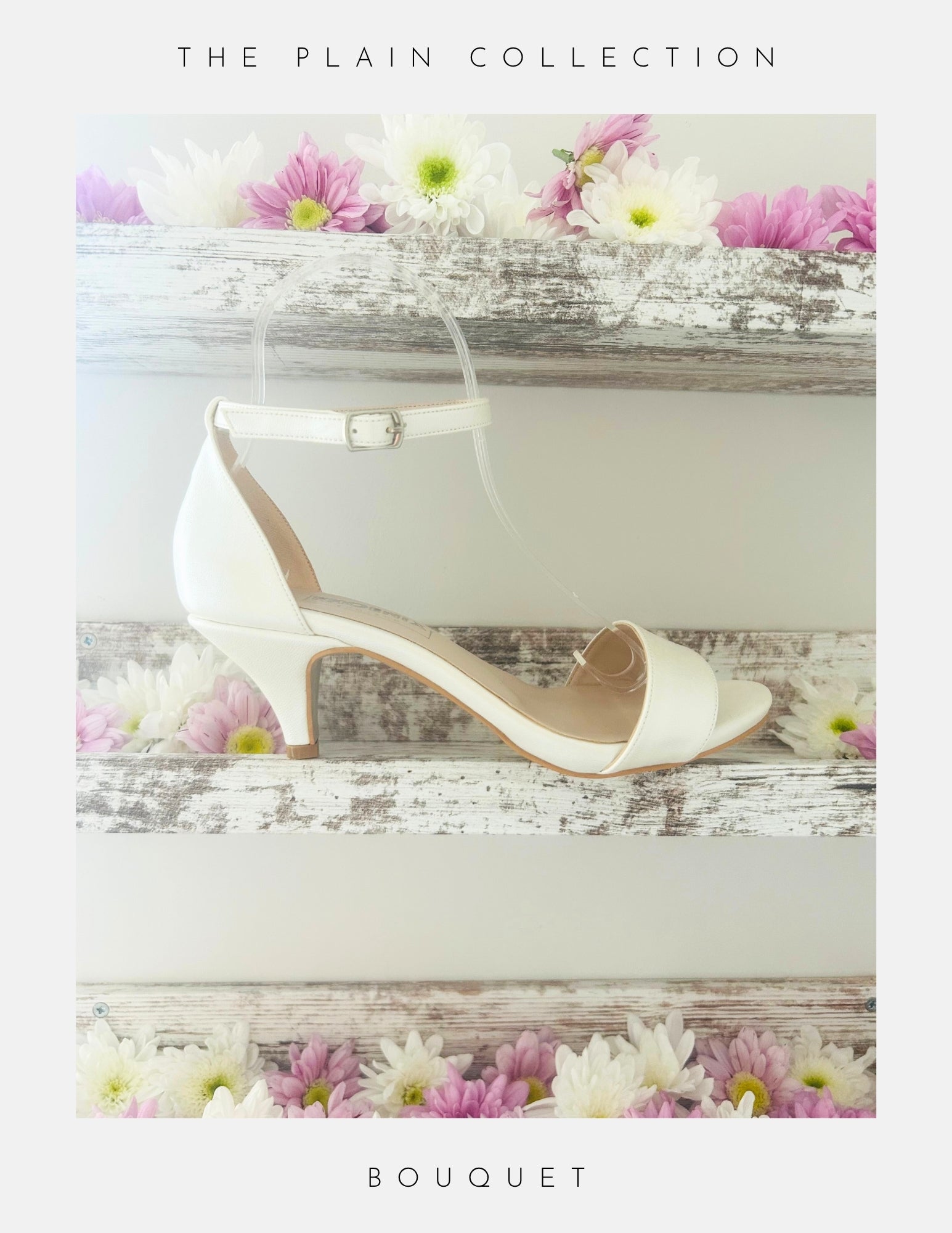 A pair of Bouquet Kitten Heel Bridal Shoes by Phoenix England in pearl vegan leather with an ankle strap rests on a rustic white shelf, surrounded by pink and white daisies. The Plain Collection—perfect bridal heels for your special day.