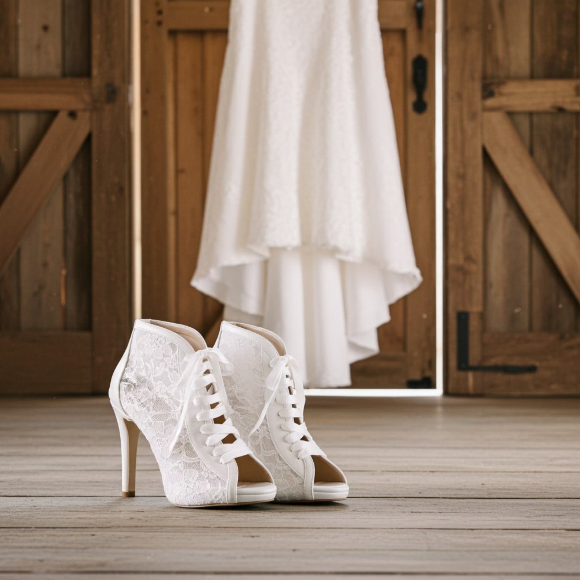 Ivory lace high-heeled shoes on a wooden floor with a white dress hanging in the background.