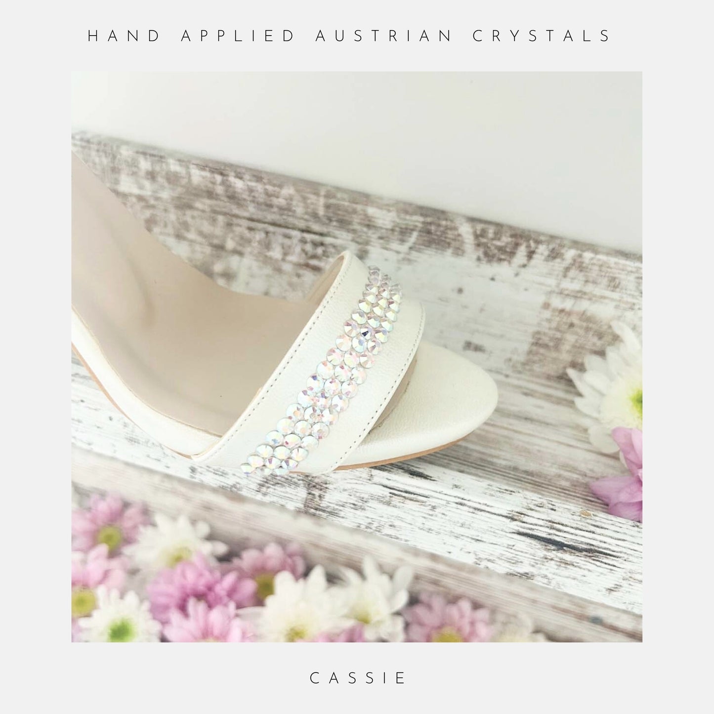 Ivory sandal with crystal embellishments on a wooden surface with flowers.