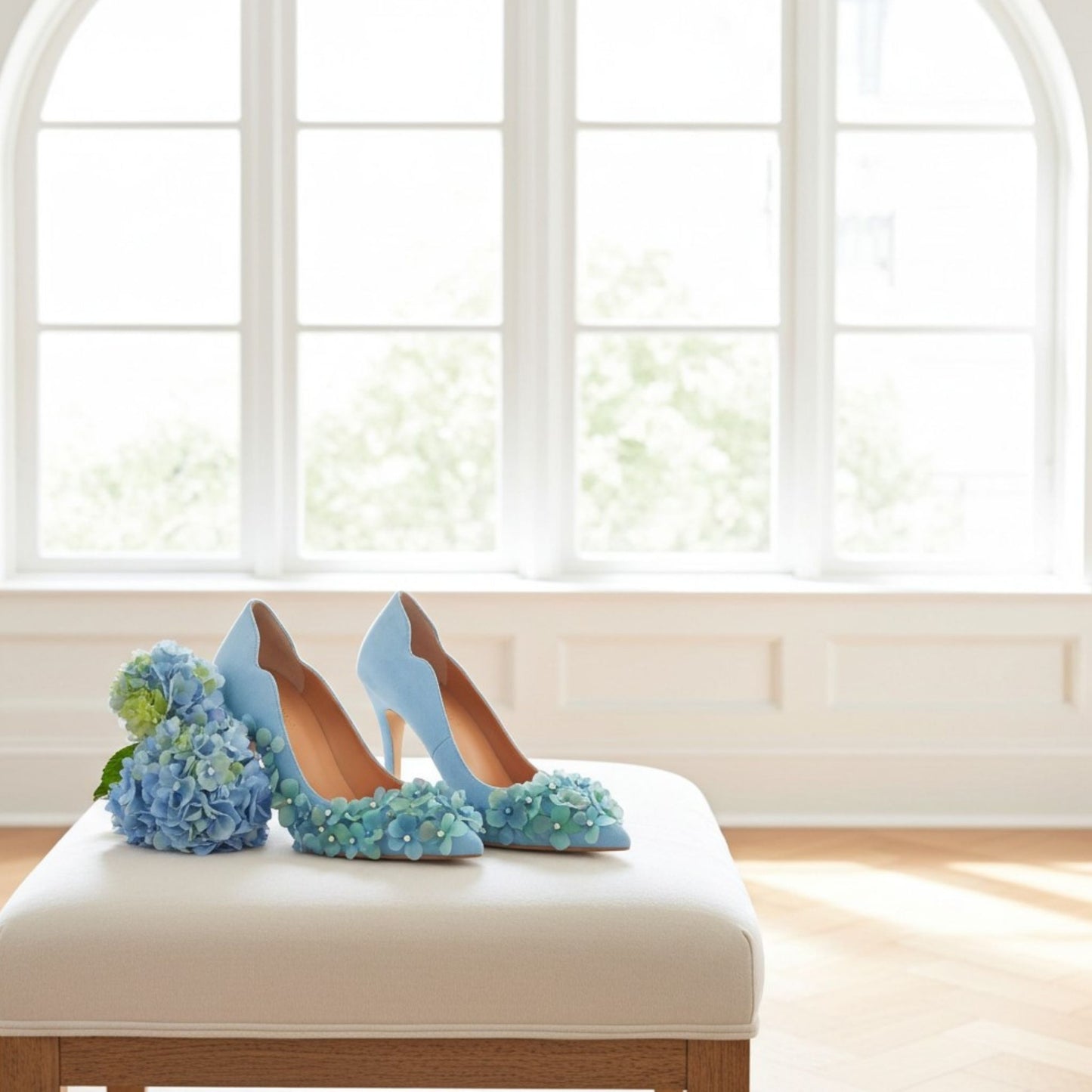 Blue high-heeled wedding shoes with floral details on a white cushion in front of a window.