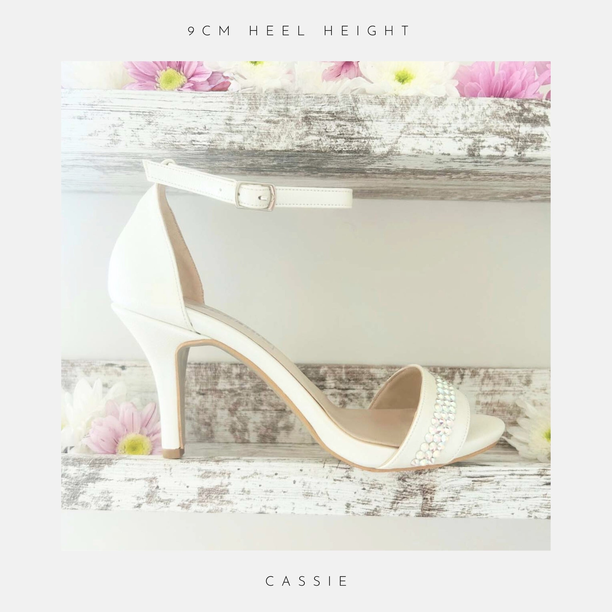 Ivory bridal sandal with crystals on a wooden surface with flowers, labelled 'Cassie' from 'The Crystal Collection'.