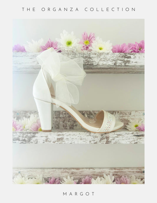 Ivory sandal with an organza bow on a wooden surface with flowers