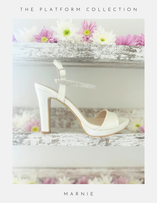 Ivory high-heeled bridal sandal with a platform on a decorative surface with flowers.