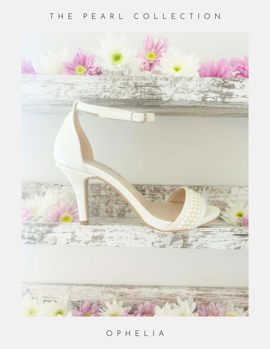 The Ophelia Pearl High Heel Wedding Shoes by Phoenix England are displayed on a rustic white shelf with pink and white daisies. Crystal pearls adorn the front strap. Text reads: The Pearl Collection and Ophelia—perfect bridal shoes.