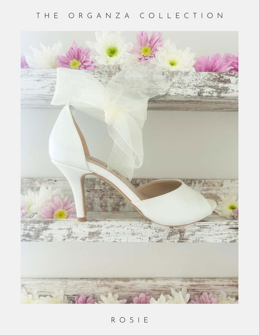 Ivory wedding shoe with floral decorations on a wooden surface with flowers.
