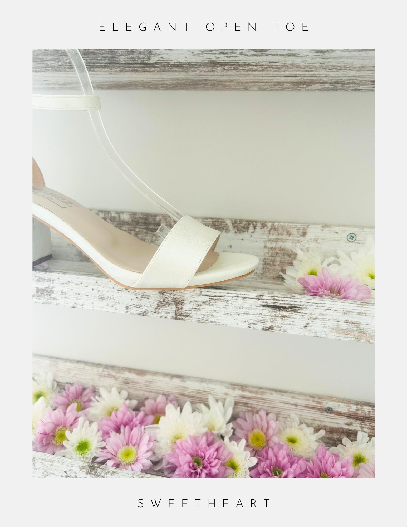 Close up of front of open toe wedding sandal in ivory on a wooden surface with flowers